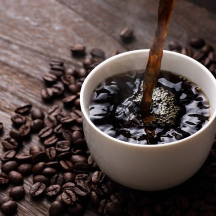coffee being poured into cup surrounded by beans