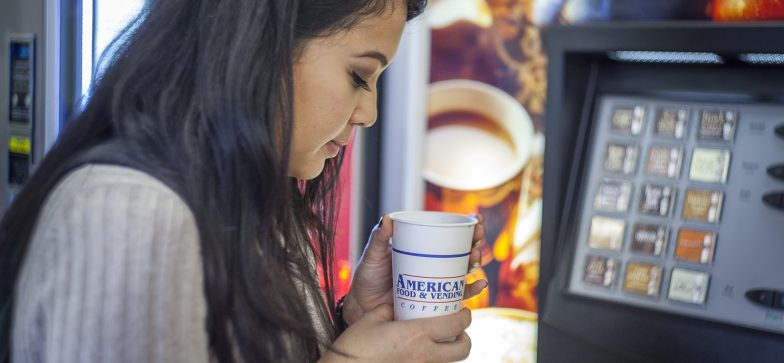 girl with coffee in front of coffee vending machine
