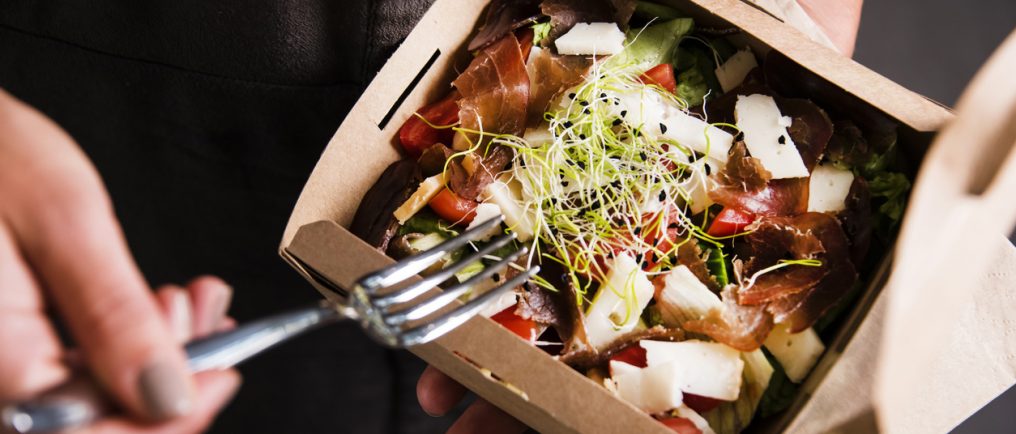 woman's hand is holding a take away fresh salad in a lunch box