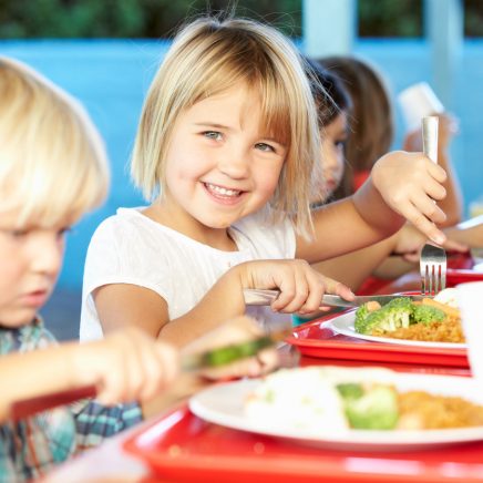 young girl cutting chicken and broccoli in cafeteria