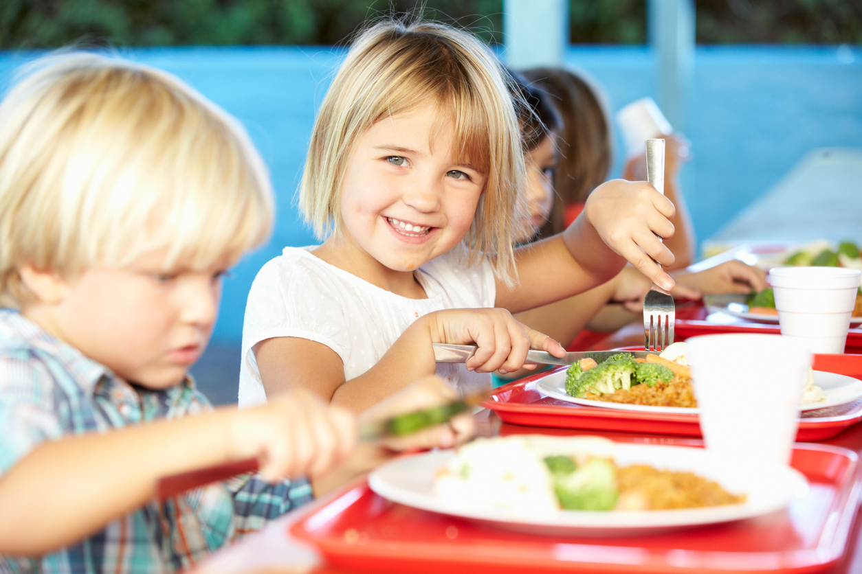 young girl cutting chicken and broccoli in cafeteria