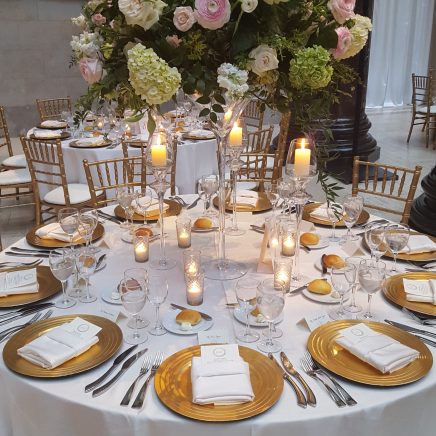 gold plates and polished silver utensils set at a circle table with a floral center piece