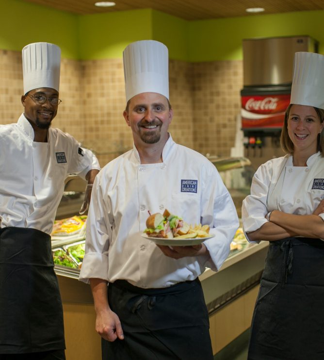 Three chefs stand in front of the freshly prepared lunch bar