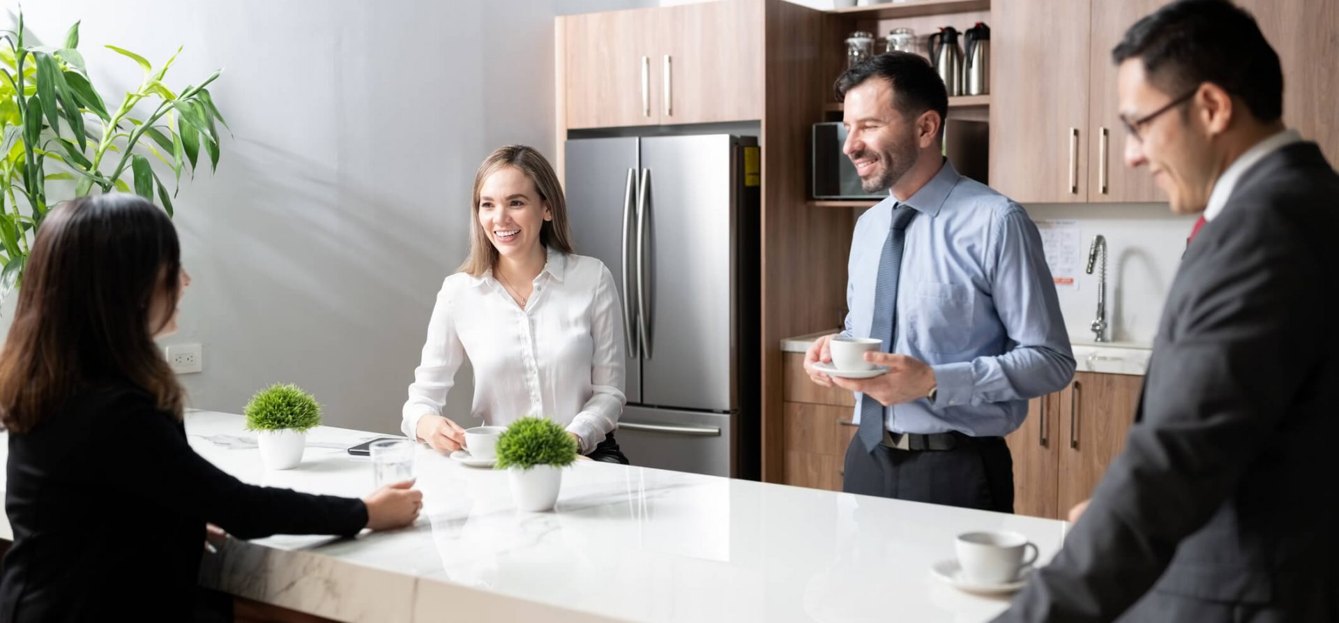 Four people in business attire gather in a breakroom to enjoy coffee
