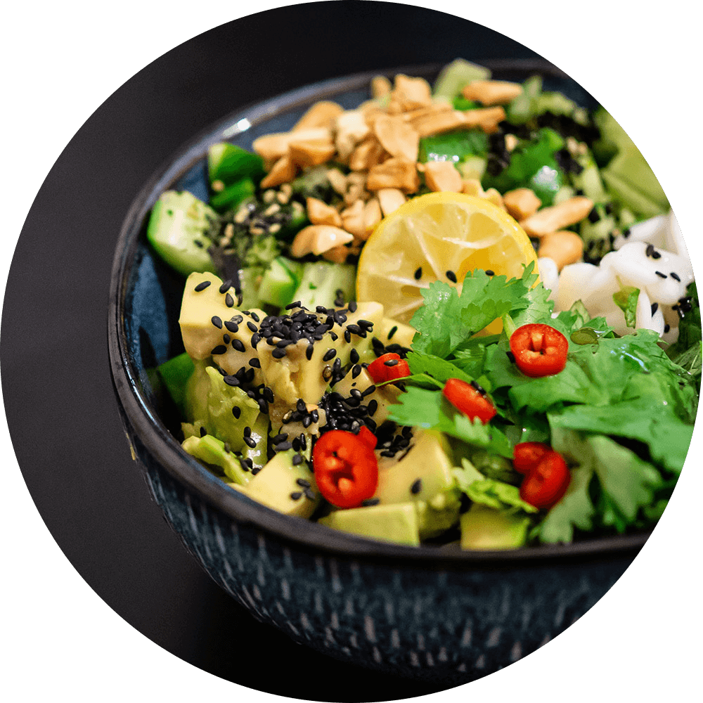 Bowl of salad filled with leafy greens, parsley, peppers, lemon, seeds, squash, avocado, and more