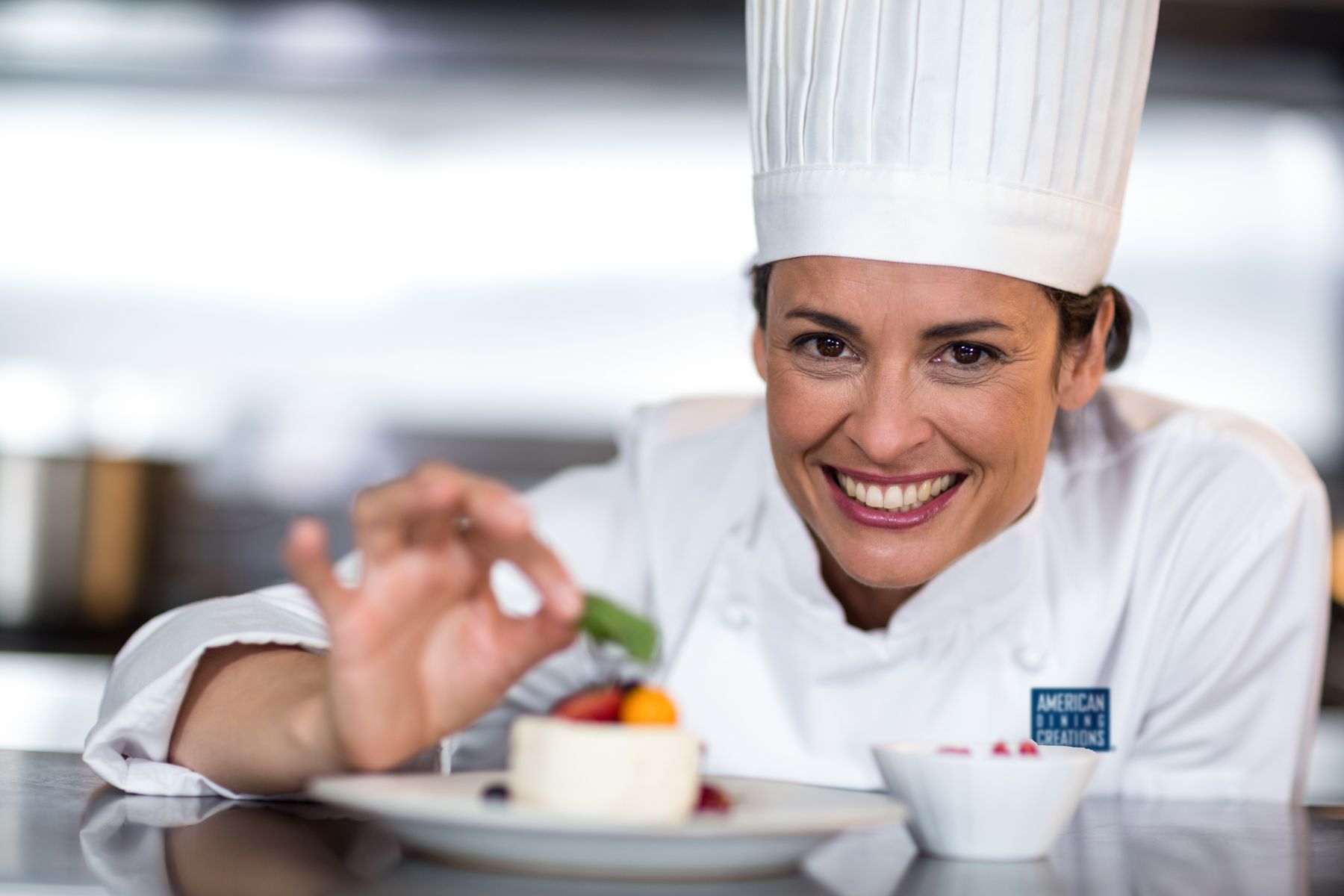 Smiling female chef plates the final touches on fruit dish