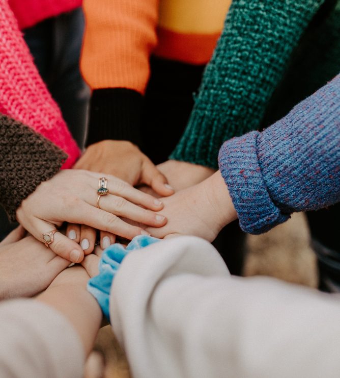Gathering of hands stacked from women wearing colorful sweaters