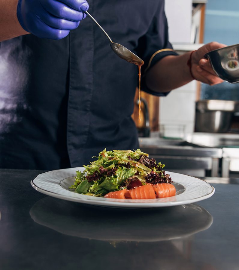 A chef puts the final touches on a salad by drizzling dressing over the bed of greens