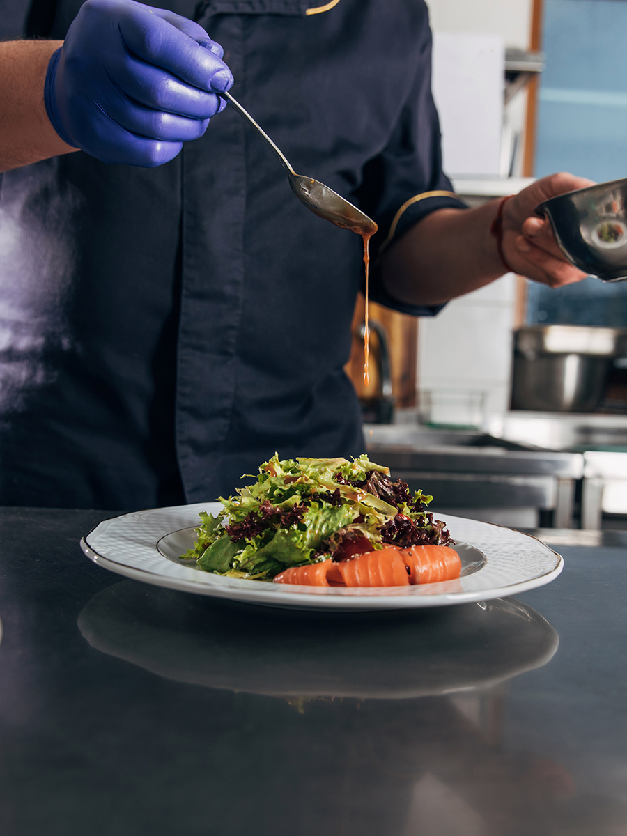 A chef puts the final touches on a salad by drizzling dressing over the bed of greens